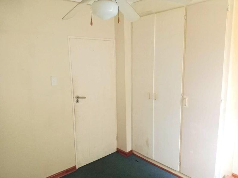A vacant bedroom featuring built-in cupboards, a ceiling fan, and carpeted flooring, presenting a blank canvas for potential renovation or restyling.
