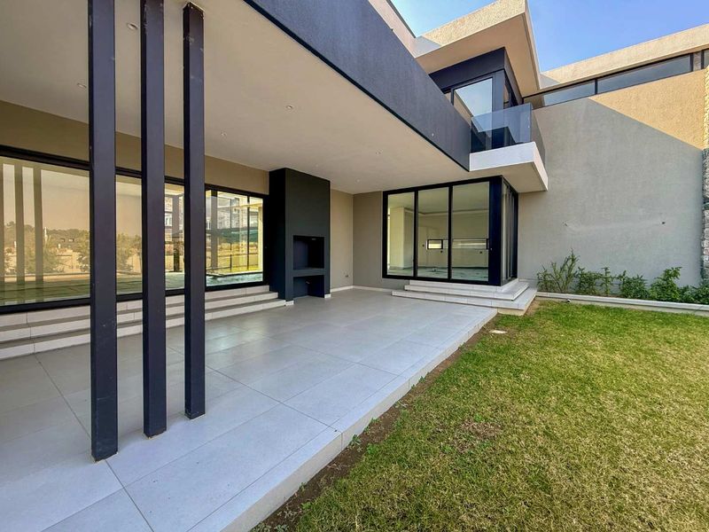Modern covered patio featuring large format floor tiles, a built-in braai, and seamless access to the garden through expansive sliding glass doors.