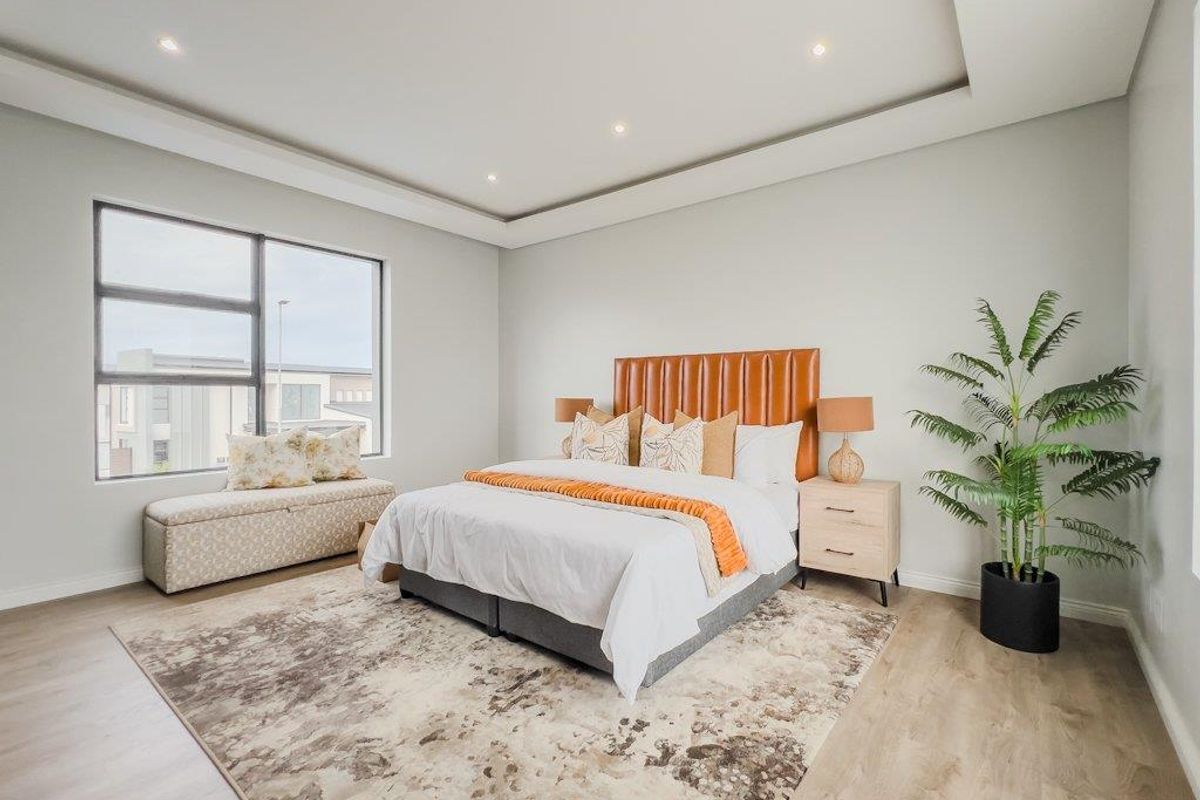 A spacious, modern bedroom featuring recessed ceiling lighting, large windows with a built-in window seat, and light-toned wood-look flooring.