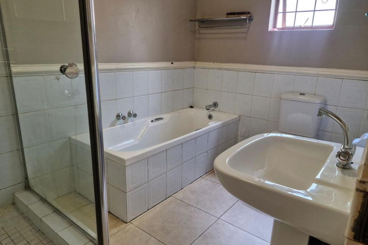 A functional bathroom featuring a tiled bathtub, a separate glass-enclosed shower, a pedestal basin, and a toilet with neutral wall finishes.