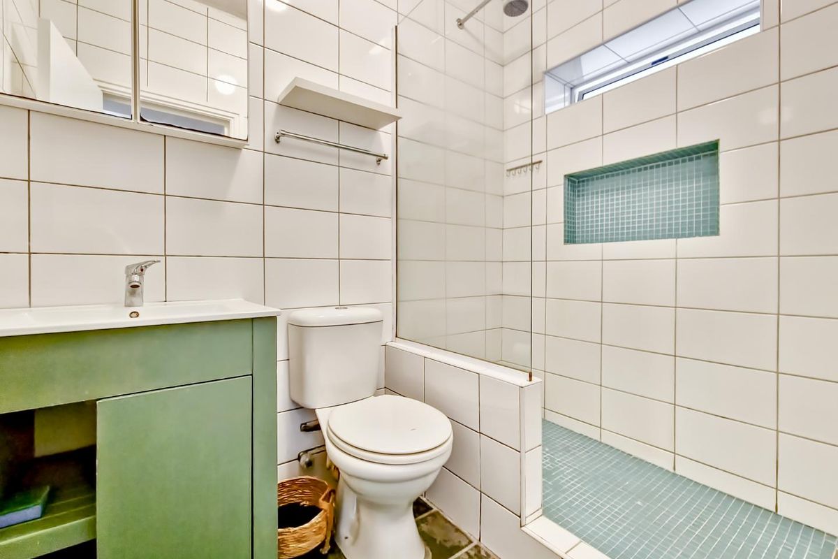 A functional bathroom featuring a green vanity, white wall tiles, a walk-in shower with a mosaic-tiled niche, and a mirrored medicine cabinet.