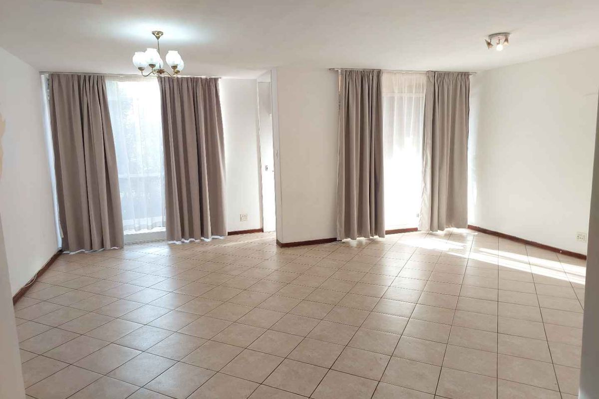 Spacious, light-filled living area featuring neutral ceramic floor tiles and large windows with curtain tracks, offering a blank canvas for interior design.