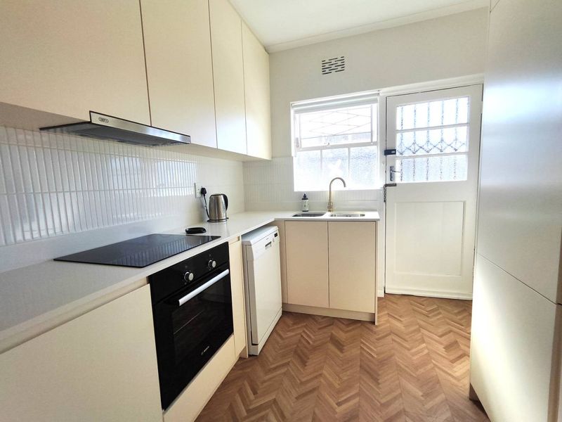 Modern kitchen featuring sleek cabinetry, herringbone flooring, integrated appliances including an oven and hob, and direct access to an exterior door.