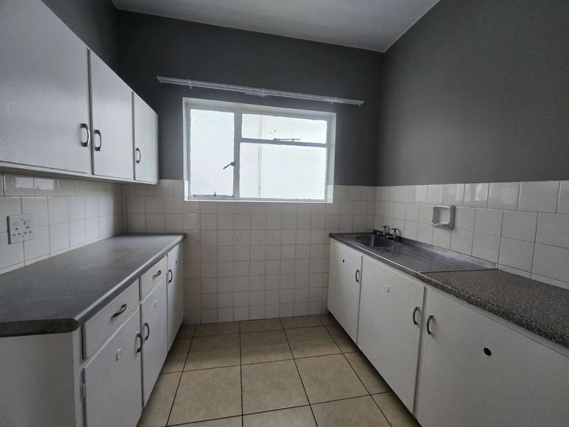 A functional, empty kitchen featuring white built-in cabinetry, laminate countertops, a stainless steel sink, and tiled backsplash, ready for modernization.
