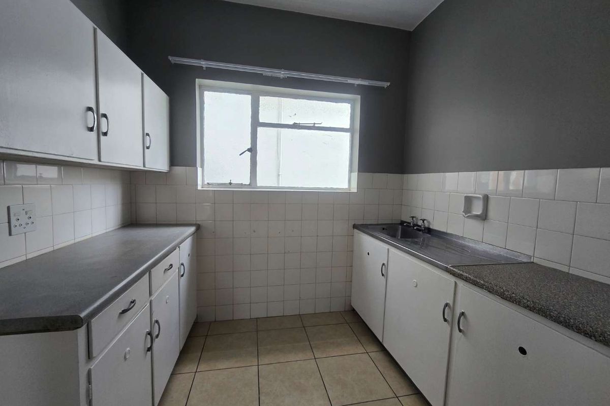 A functional, empty kitchen featuring white built-in cabinetry, laminate countertops, a stainless steel sink, and tiled backsplash, ready for modernization.