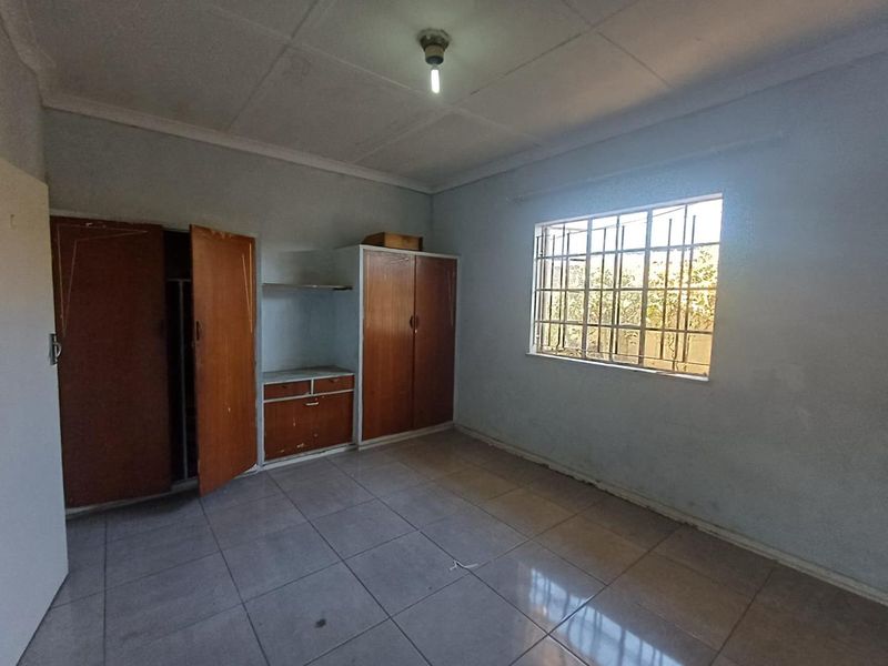 A vacant bedroom featuring tiled flooring, built-in wooden cupboards, and a window fitted with security bars.