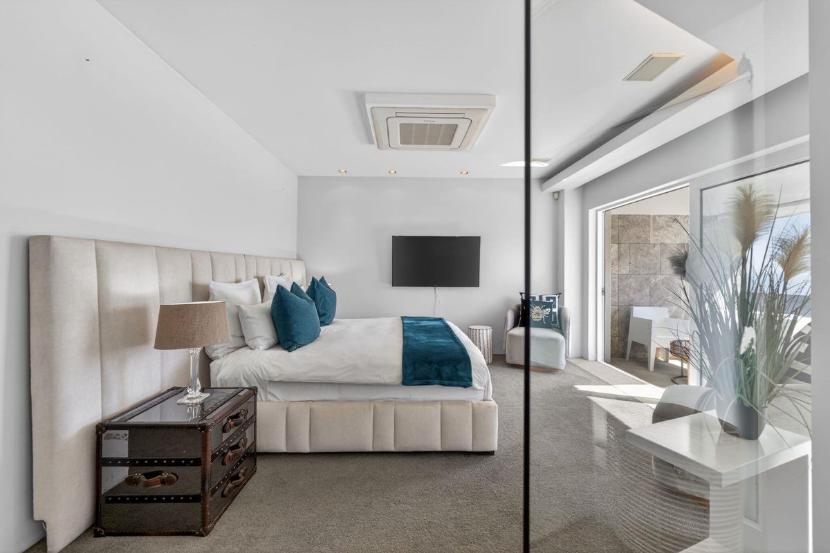 Spacious modern bedroom featuring a ceiling-mounted air conditioning unit, recessed lighting, and large sliding glass doors leading to a private balcony.