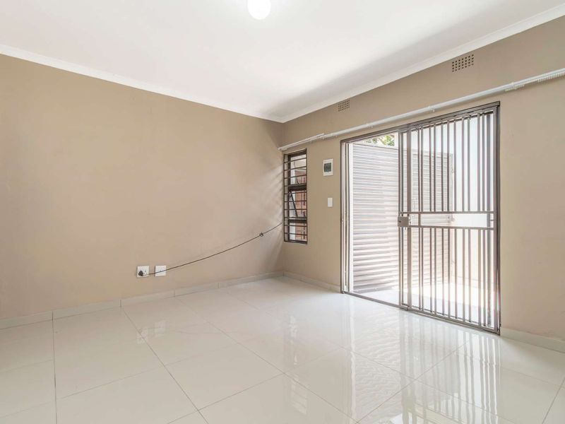 A bright, empty living area featuring neutral walls, polished tiled flooring, and a sliding glass door with a security gate leading outdoors.