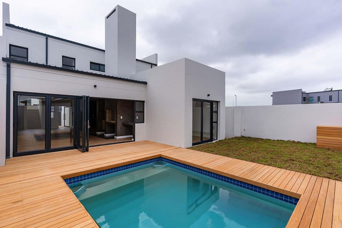 Modern rear exterior featuring a swimming pool with timber decking, bi-fold doors leading to an indoor living area, and a built-in braai.