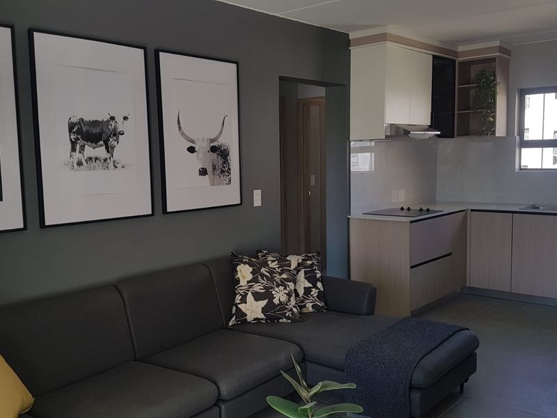Modern open-plan living area featuring a contemporary kitchen with built-in cabinetry, electric hob, and sleek tiled flooring throughout.