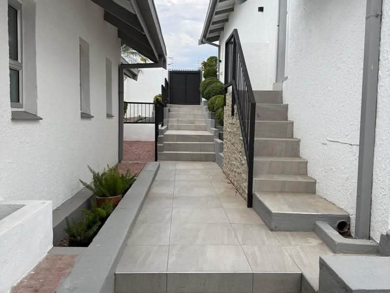 A well-maintained exterior walkway featuring tiled steps, metal handrails, and stone cladding accents, leading towards a secure rear gate.