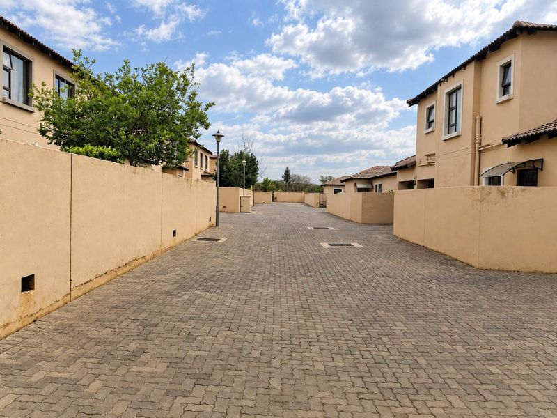 A view of the paved complex driveway flanked by townhouse boundary walls and residential units under a clear sky.