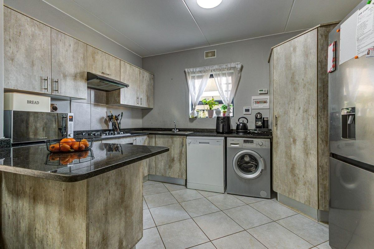 A functional kitchen featuring wood-look cabinetry, dark granite countertops, tiled flooring, and integrated space for laundry and dishwashing appliances.
