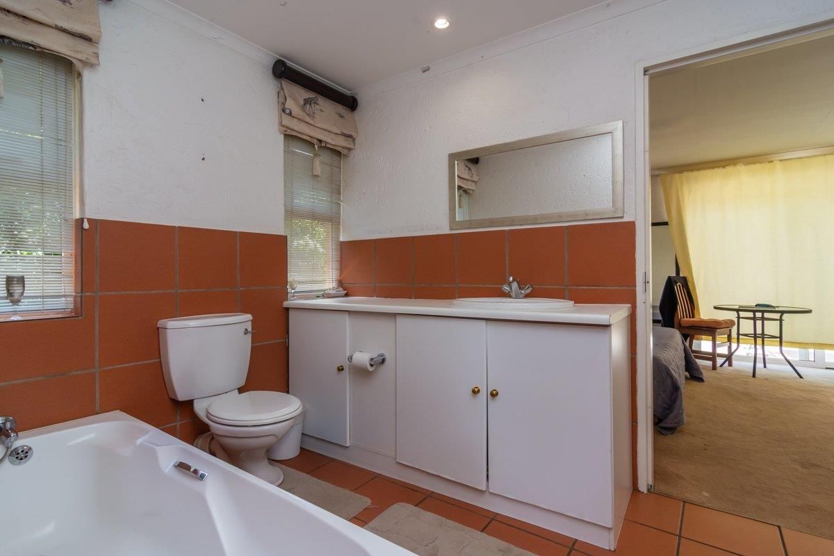 A functional bathroom featuring a built-in vanity with integrated basin, a standard toilet, and a bathtub, finished with terracotta-style wall and floor tiles.
