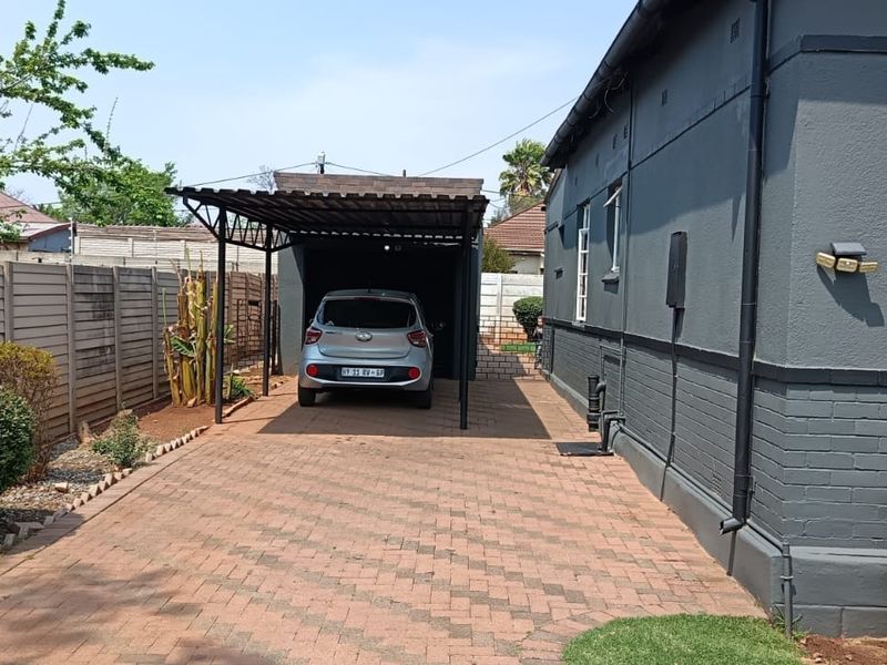 A side view of the property featuring a paved driveway leading to a covered carport, enclosed by a precast concrete boundary wall.