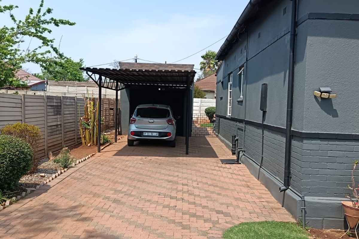 A side view of the property featuring a paved driveway leading to a covered carport, enclosed by a precast concrete boundary wall.