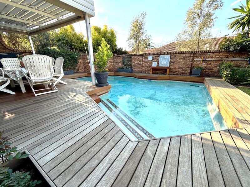 Outdoor pool area featuring timber decking, a covered patio space, and a brick boundary wall, providing a private setting for relaxation.