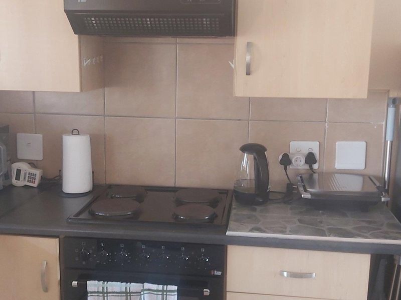 A functional kitchen featuring laminate cabinetry, a tiled backsplash, and built-in cooking appliances including an electric hob and oven.
