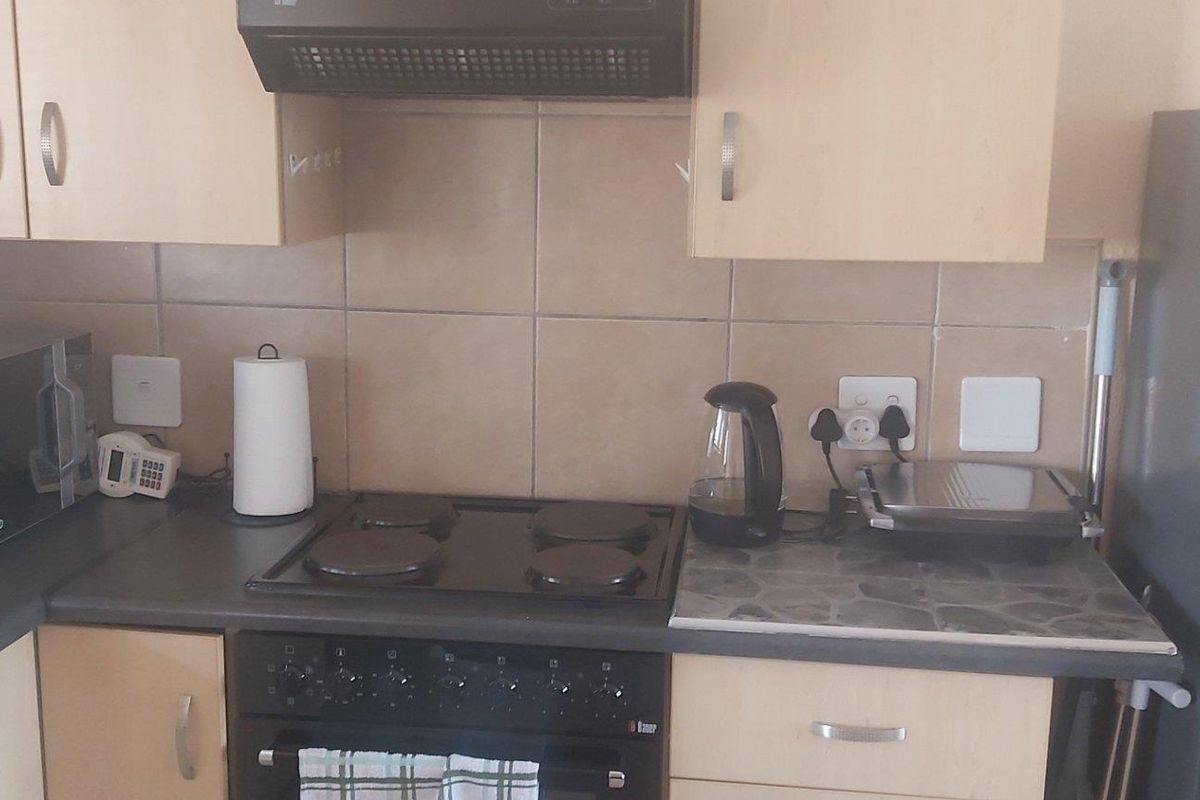 A functional kitchen featuring laminate cabinetry, a tiled backsplash, and built-in cooking appliances including an electric hob and oven.