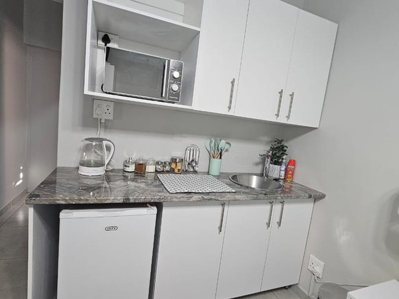 Compact kitchenette featuring white cabinetry, stone-look countertops, a stainless steel sink, and tiled flooring, providing essential food preparation space.