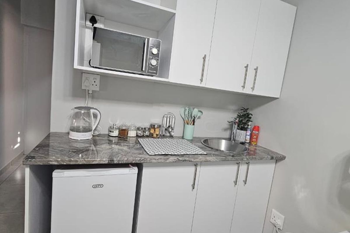 Compact kitchenette featuring white cabinetry, stone-look countertops, a stainless steel sink, and tiled flooring, providing essential food preparation space.
