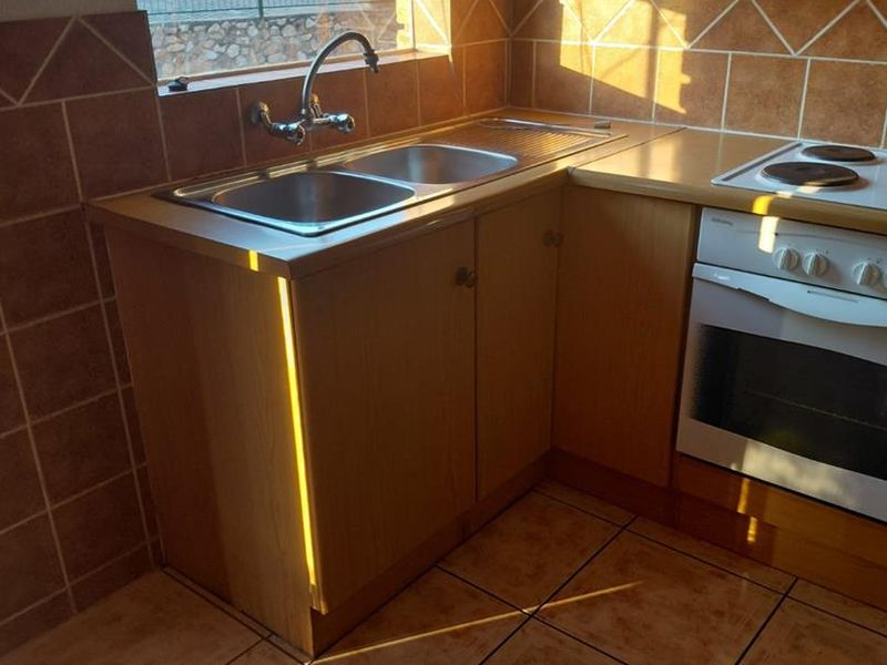 A functional kitchen featuring built-in cabinetry, a double basin sink, an integrated oven and hob, and tiled finishes throughout.