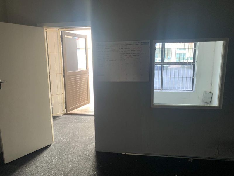 A vacant office space featuring carpeted flooring, a security gate at the entrance, and a window fitted with security bars.