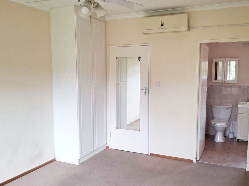 A spacious bedroom featuring a built-in wardrobe, split-system air conditioning, and an attached en-suite bathroom.