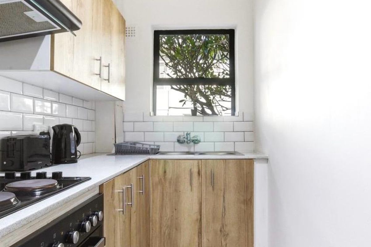 A compact, modern kitchen featuring light wood-grain cabinetry, white subway tile backsplash, a built-in oven with hob, and a stainless steel sink.