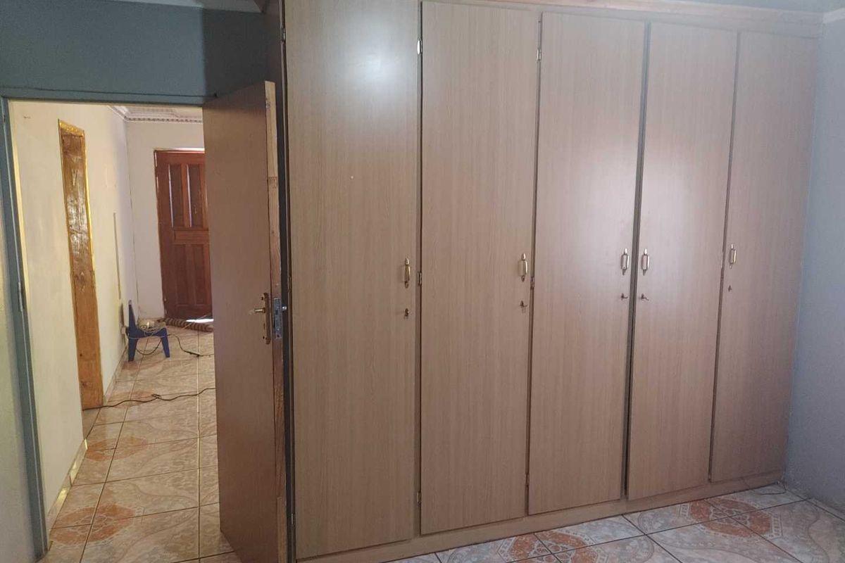 A bedroom featuring built-in wooden wardrobes and tiled flooring, with a view into the adjacent hallway.