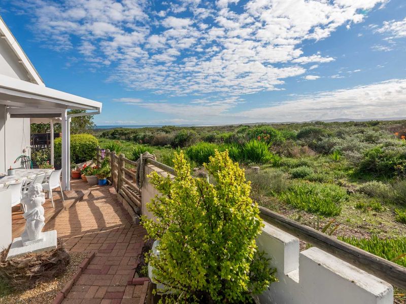 A covered patio area featuring brick paving and a wooden fence, overlooking a natural coastal landscape with expansive views.