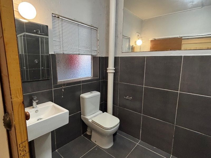 A functional bathroom featuring dark grey wall and floor tiles, a pedestal basin, toilet, and a large wall-mounted mirror.