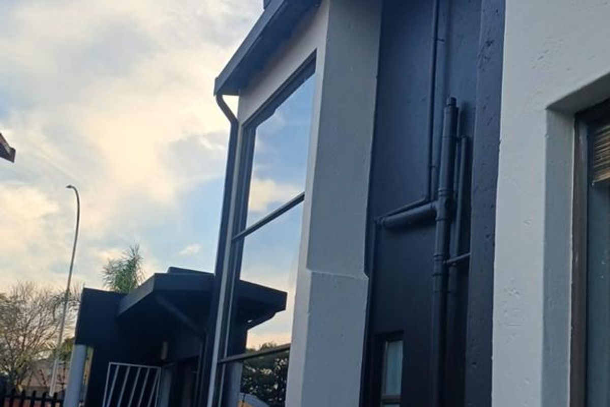 A view of the rear exterior elevation featuring modern dark and light contrasting paintwork, large windows, and paved outdoor area.