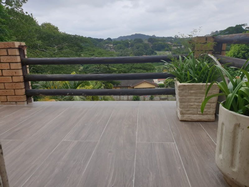 An elevated balcony featuring tiled flooring, a timber log railing, and a brick pillar, offering scenic views of the surrounding landscape.