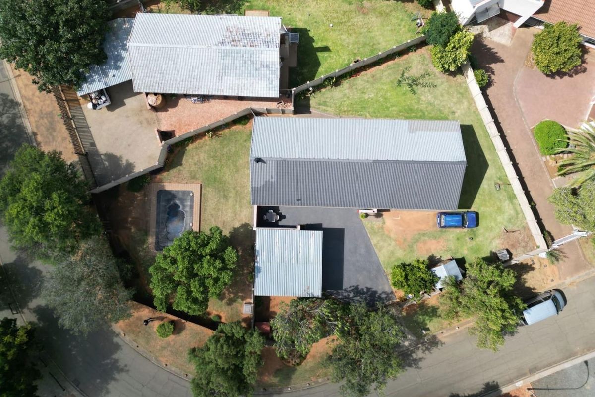 Aerial view of the property featuring a main dwelling with a metal roof, a swimming pool, and a detached outbuilding set within a landscaped garden.