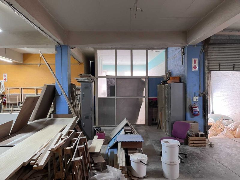 Industrial utility space featuring exposed concrete structure, metal roller shutter access, and a partitioned office area, suitable for workshop or storage use.
