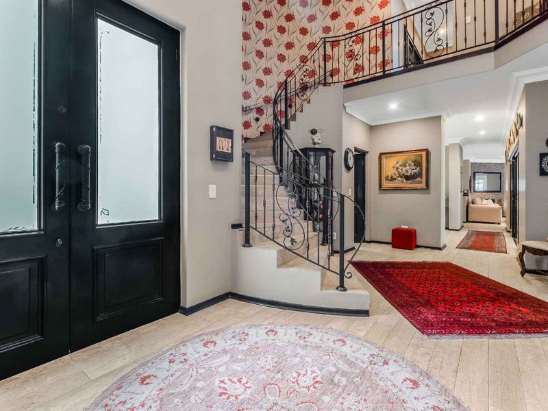 Spacious entrance hall featuring a grand staircase with wrought iron balustrades, tiled flooring, and a double front door entry.