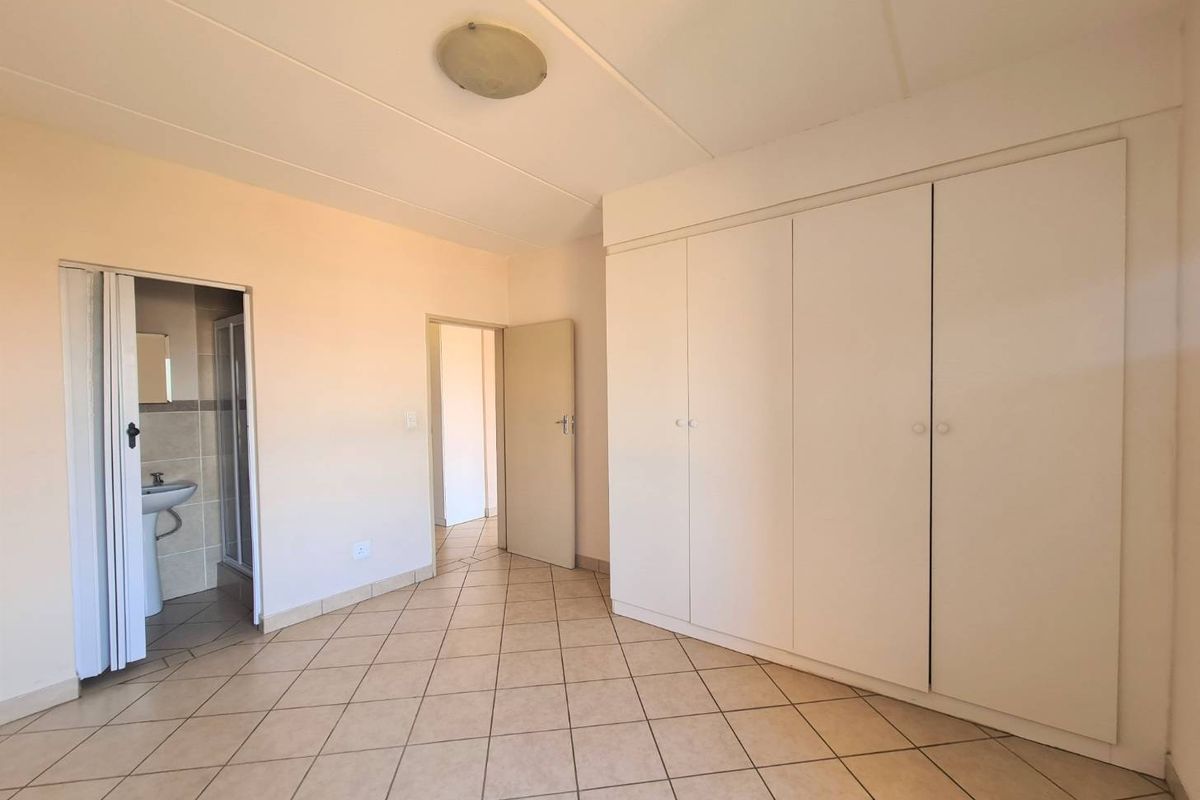 A spacious, empty bedroom featuring neutral tiled flooring, ample built-in cupboard storage, and direct access to an en-suite bathroom.