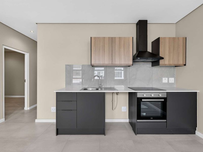 Modern kitchen featuring sleek dark cabinetry, light wood-tone upper cabinets, stone countertops, integrated oven, hob, and extractor fan with a clean tiled backsplash.