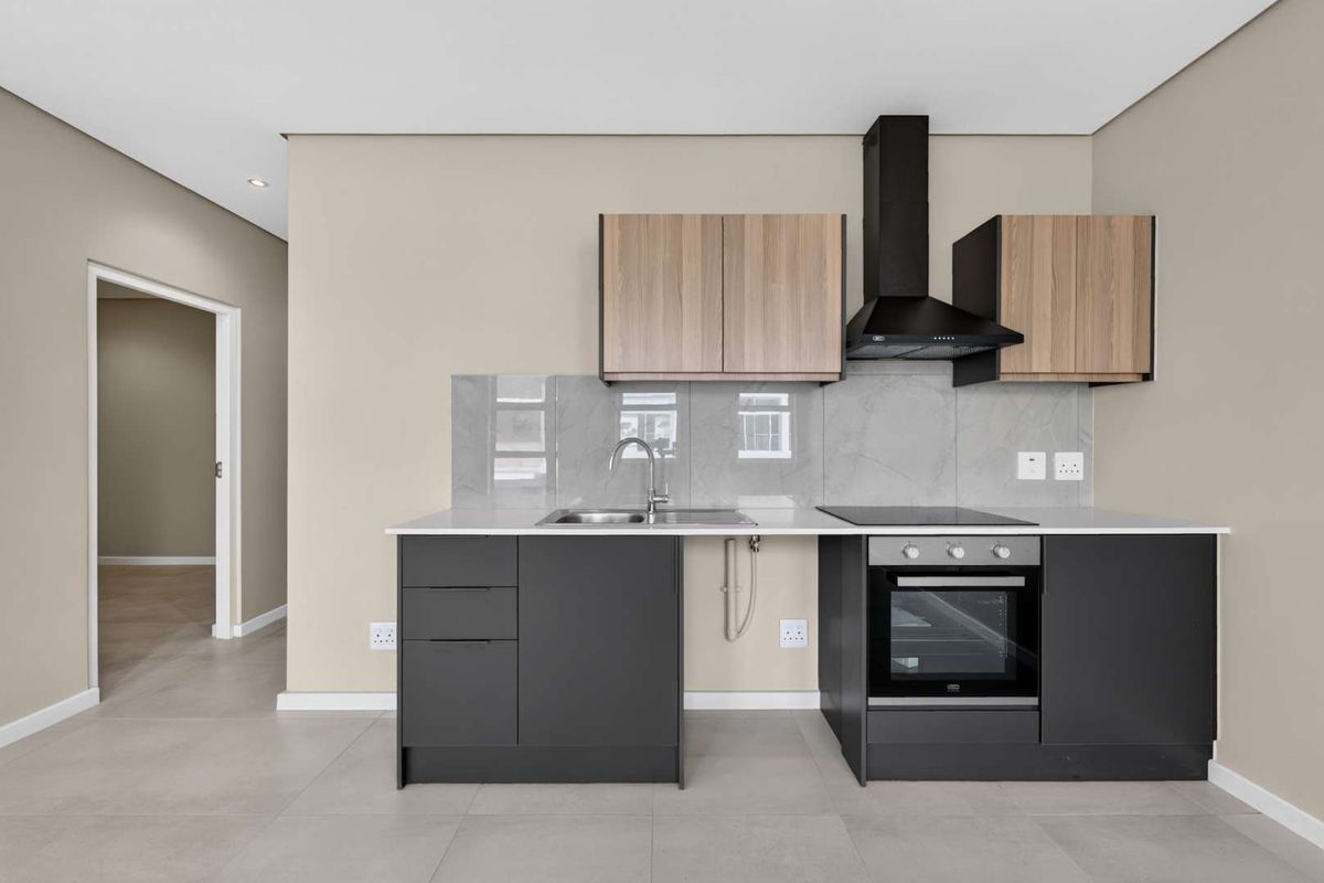 Modern kitchen featuring sleek dark cabinetry, light wood-tone upper cabinets, stone countertops, integrated oven, hob, and extractor fan with a clean tiled backsplash.