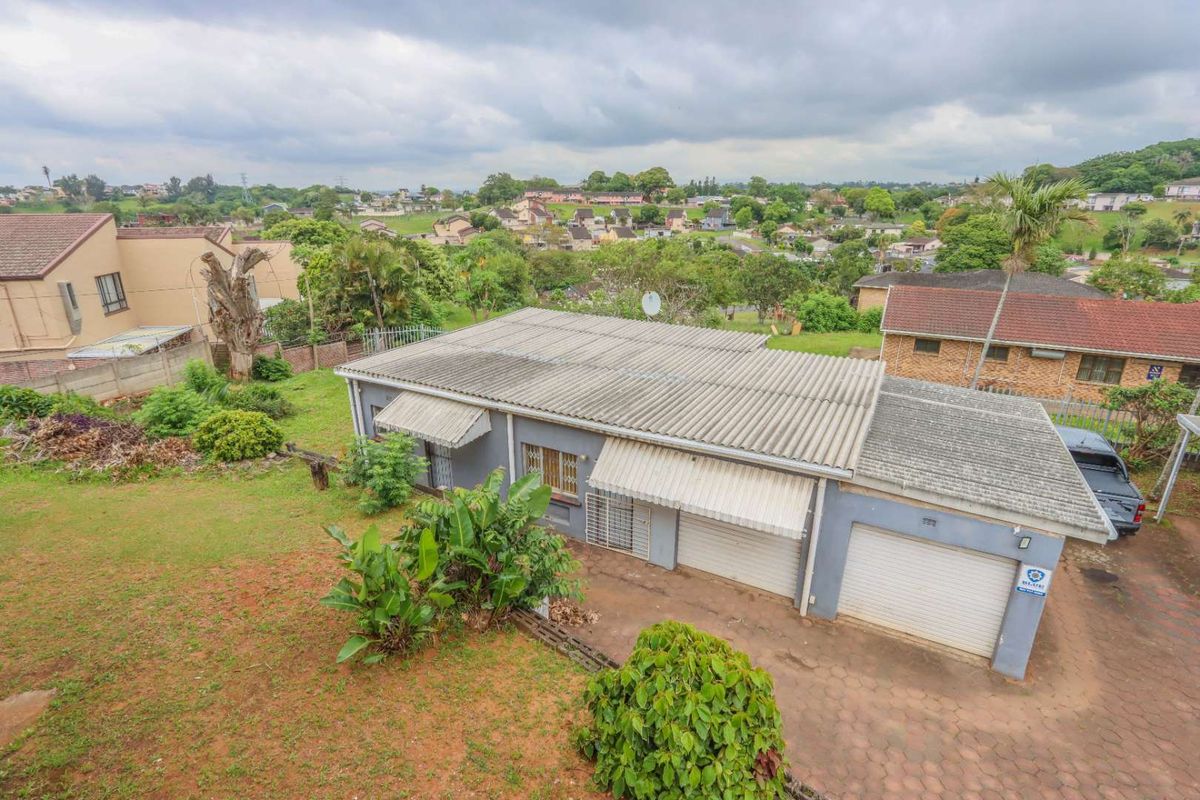 Aerial view of a residential property featuring a double garage, corrugated roof, and surrounding garden space in a suburban neighborhood setting.