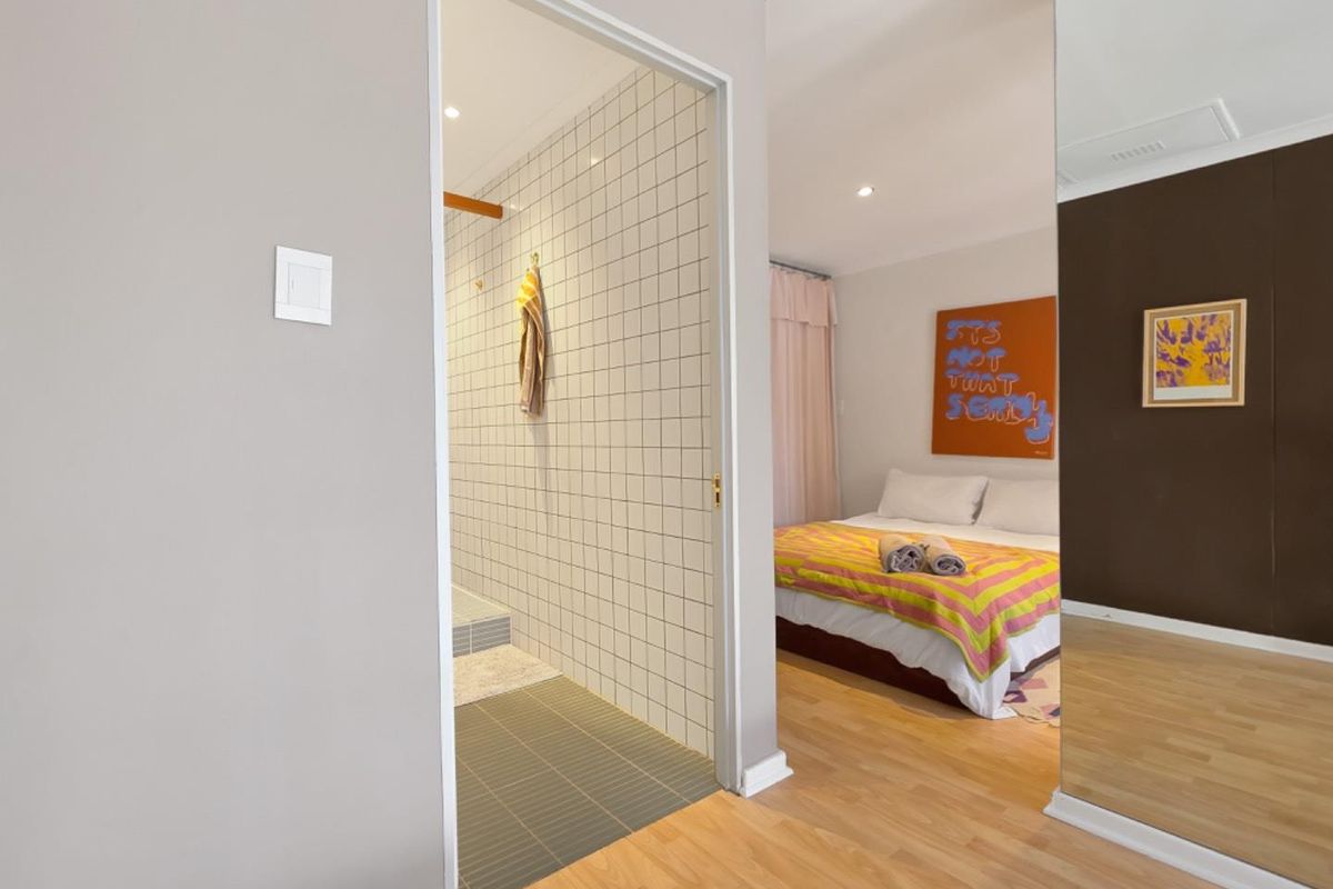A well-maintained bedroom featuring laminate flooring, recessed lighting, and mirrored wardrobe doors, with an adjoining tiled bathroom visible through the doorway.