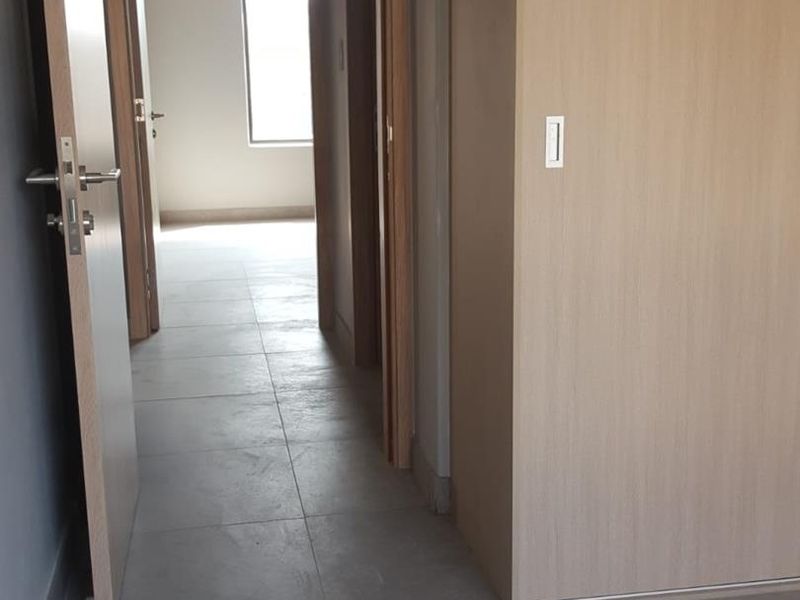 A clean, modern hallway featuring neutral tiled flooring and built-in wooden cabinetry, leading towards an open room with natural light.
