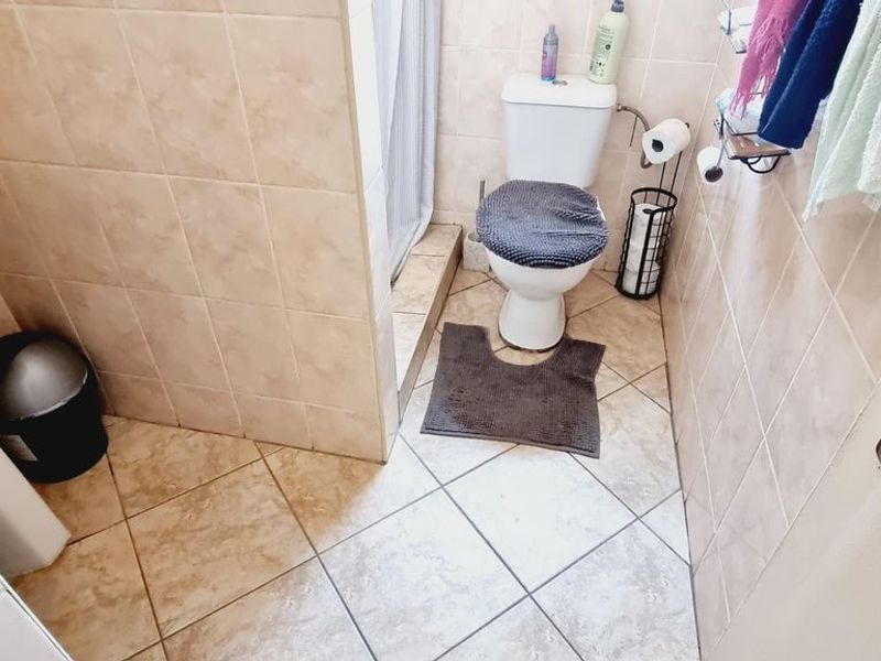 A functional bathroom featuring a pedestal washbasin, toilet, and a shower enclosure with tiled walls and flooring.