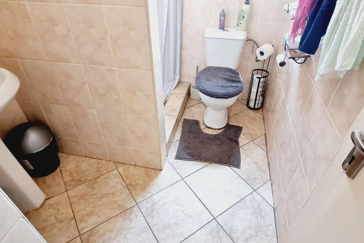A functional bathroom featuring a pedestal washbasin, toilet, and a shower enclosure with tiled walls and flooring.