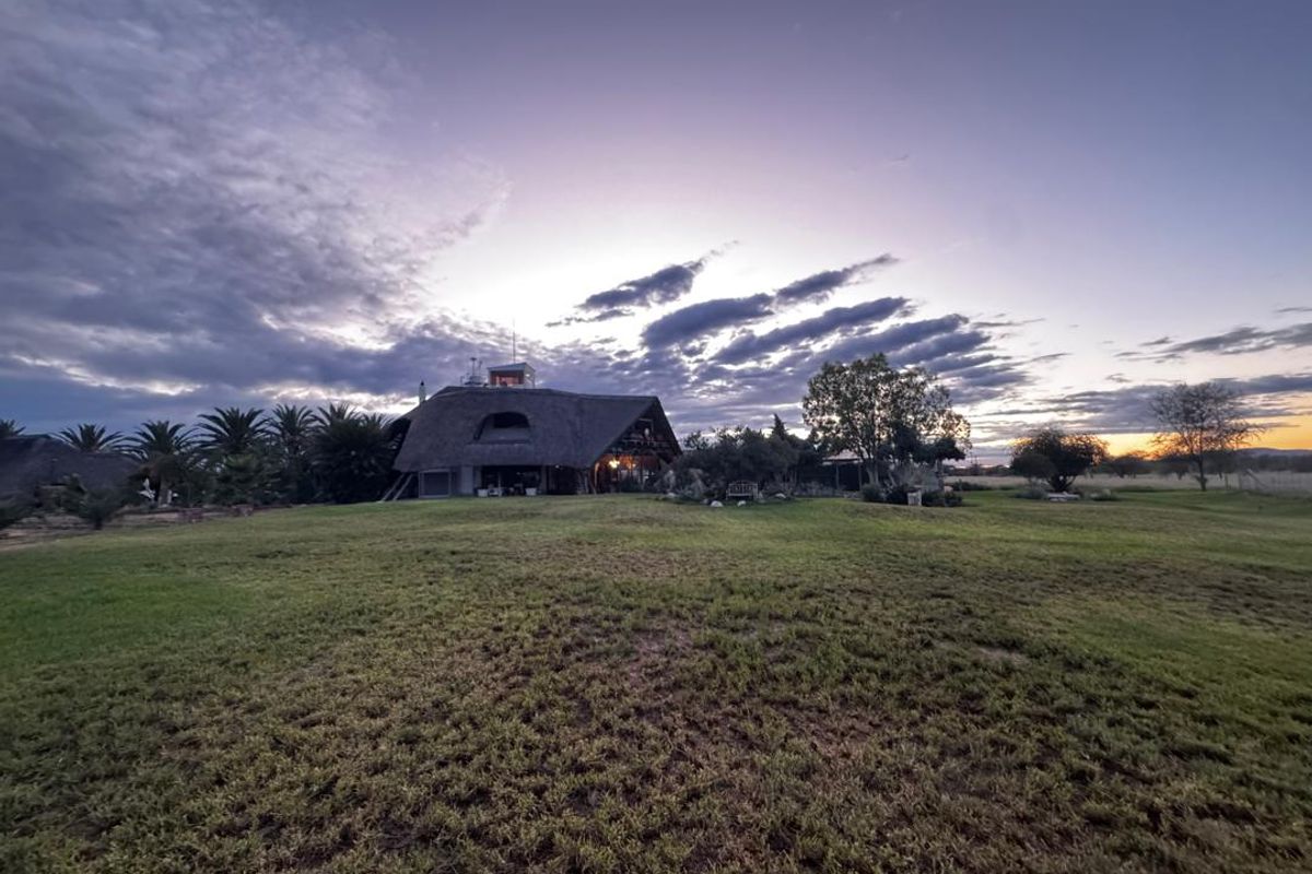 A wide-angle view of the farm property at dusk, showcasing the main thatched-roof dwelling set within expansive landscaped grounds.