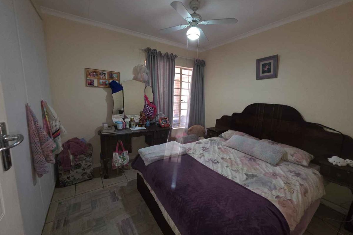 A functional bedroom featuring tiled flooring, a ceiling fan, and built-in storage cupboards.