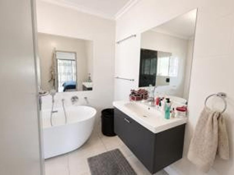 Modern bathroom featuring a sleek freestanding bathtub, a wall-mounted vanity with an integrated basin, and a large mirror, creating a clean and functional space.