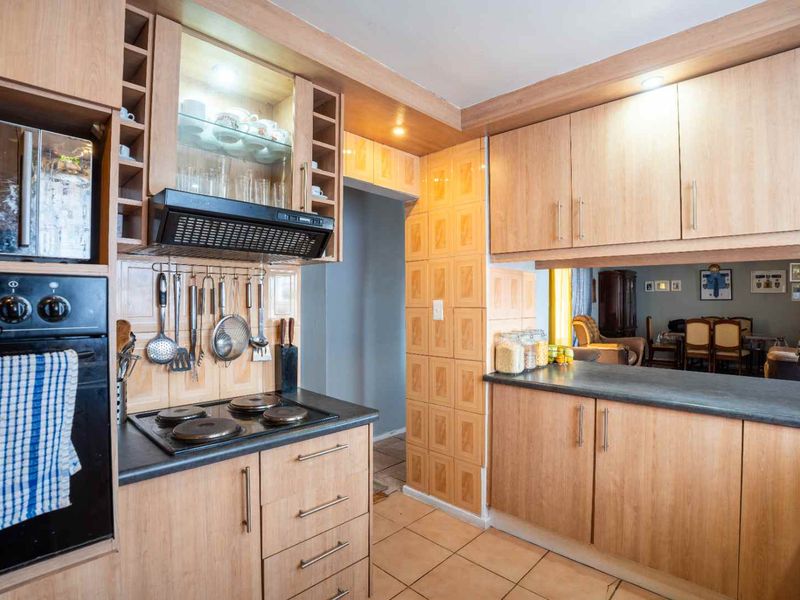 Functional kitchen featuring light wood cabinetry, dark laminate countertops, built-in oven, electric hob, and tiled flooring with an open-plan layout to the dining area.