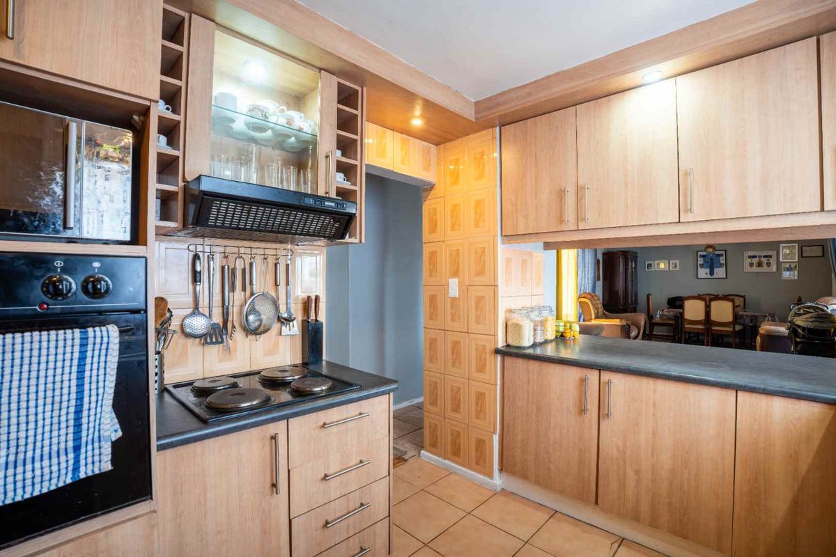 Functional kitchen featuring light wood cabinetry, dark laminate countertops, built-in oven, electric hob, and tiled flooring with an open-plan layout to the dining area.